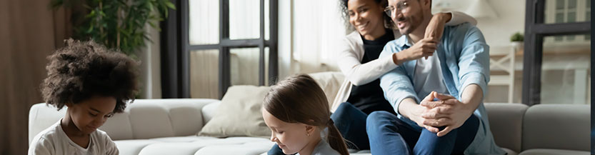 A picture of a family with parents and two children sitting in a loungeroom